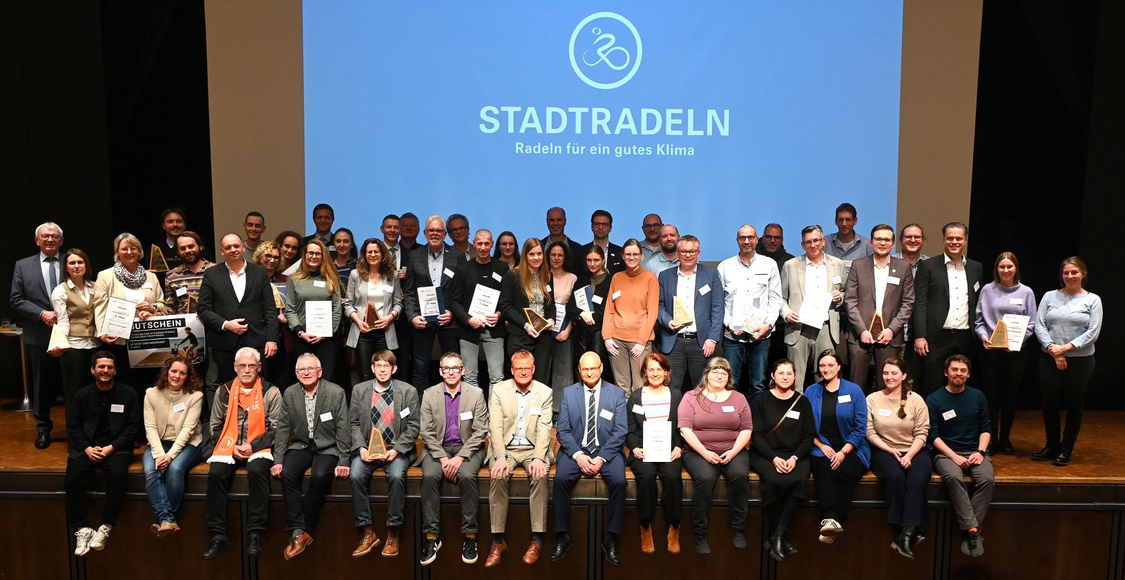 Viele Menschen stehen auf der Bühne. Auf der Leinwand im Hintergrund ist das Logo „STADTRADELN“ zu sehen.